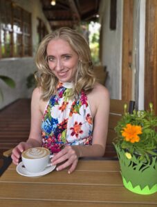 Author Rose Ford sitting at a bistro table with a cappuccino and wearing a colorful floral romper